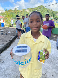 Young student holding solar lantern that says "Solcius" standing outside in a school playground.